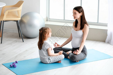 年轻孕妇和女儿在家做瑜伽图片