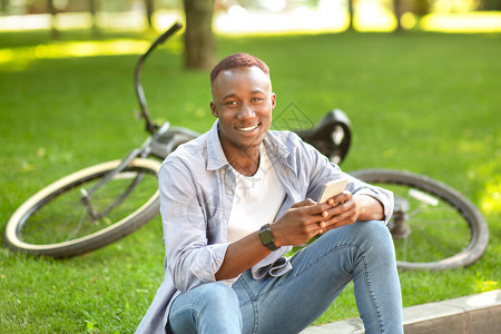 黑人在城市公园的自行车附近使用手图片