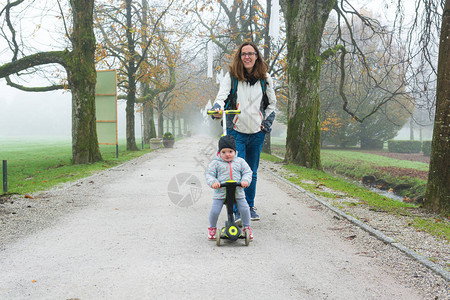 你母亲和她女儿一起在公园骑着小摩托车走在雾天下为人图片