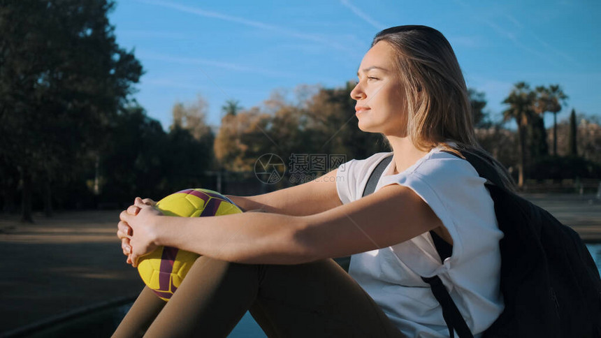 美丽的运动女孩的侧面景色背包和橄榄球在训练后梦寐以求地在城图片