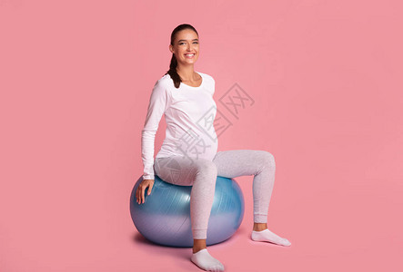 怀孕和健康坐在健身球上微笑的孕妇在摄影机里图片
