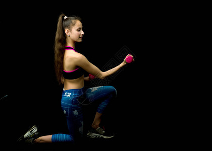 一个抱着哑铃的少女在健身俱乐部进行锻炼运动的概念和年轻一代的健康生图片