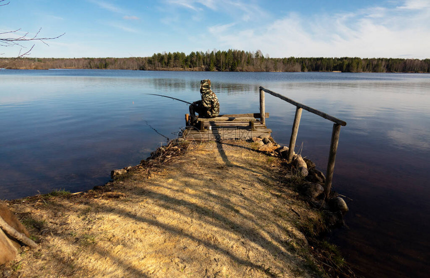 伪装的渔夫在湖岸边用浮标在水面上钓鱼一个少年坐在河岸上图片