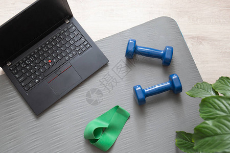 两个用于在家健身的哑铃和一台用于远程训练的笔记本电脑图片