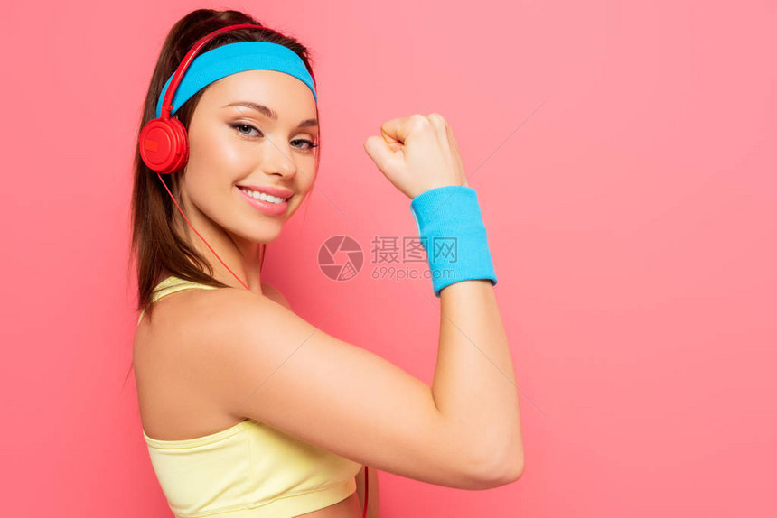 手持耳机的快乐运动女运动员在观看粉红背景相机的同时图片