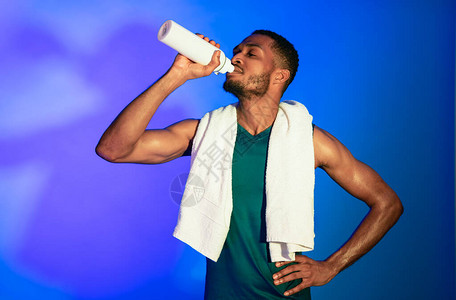锻炼补水黑色健身家伙训练后站在蓝色背景上喝图片