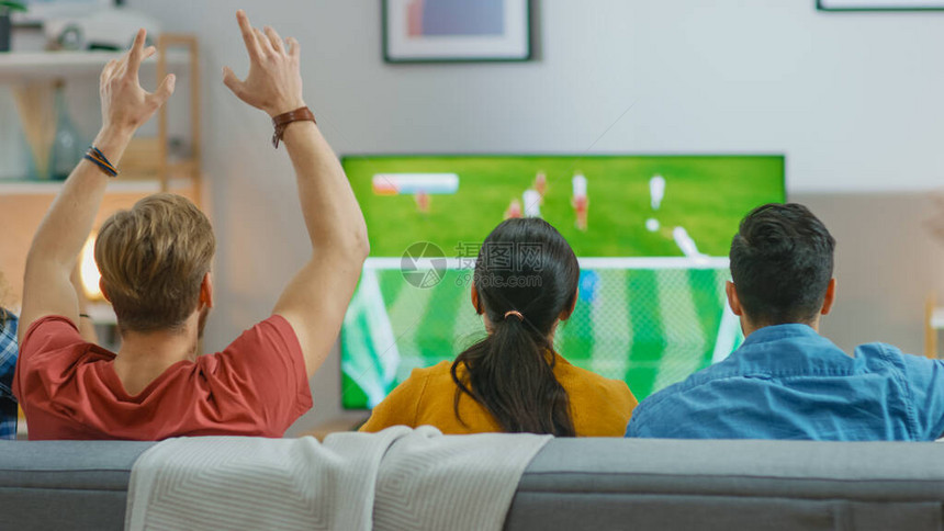 一群不同的体育迷坐在沙发上观看电视上的重要足球比赛图片