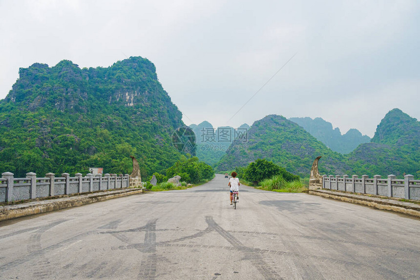 在岩石尖峰和绿色山谷之间风景秀丽的道路上独自骑行车的女人越南TrangAnNinhBinh的独特景观保持社交距离独自旅行图片