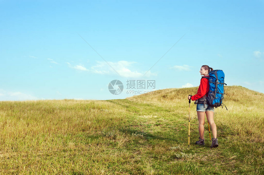 带着背包和徒步高杆在草地足迹上行走的图片