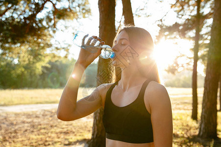 体育女青年在户外公园跑步后喝瓶装水的侧面图片