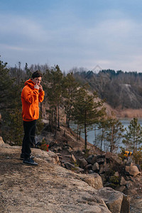 一个站在悬崖边上的年轻人在湖的背景上图片