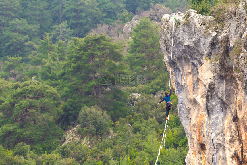 一个女人正沿着一条拉长的吊索行走山中的高线女人抓住了平衡走钢丝者在大图片