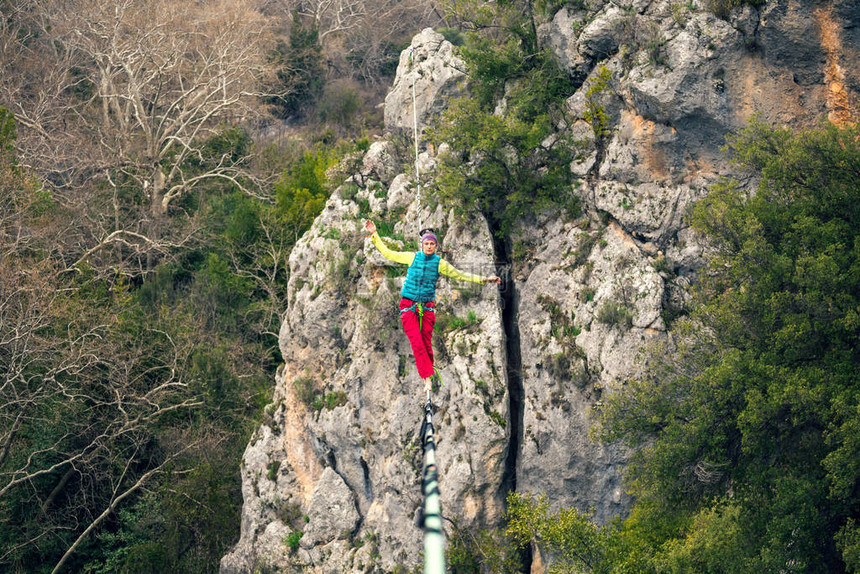 一个女人正沿着一条拉长的吊索行走山中的高线女人抓住了平衡走钢丝者在大图片