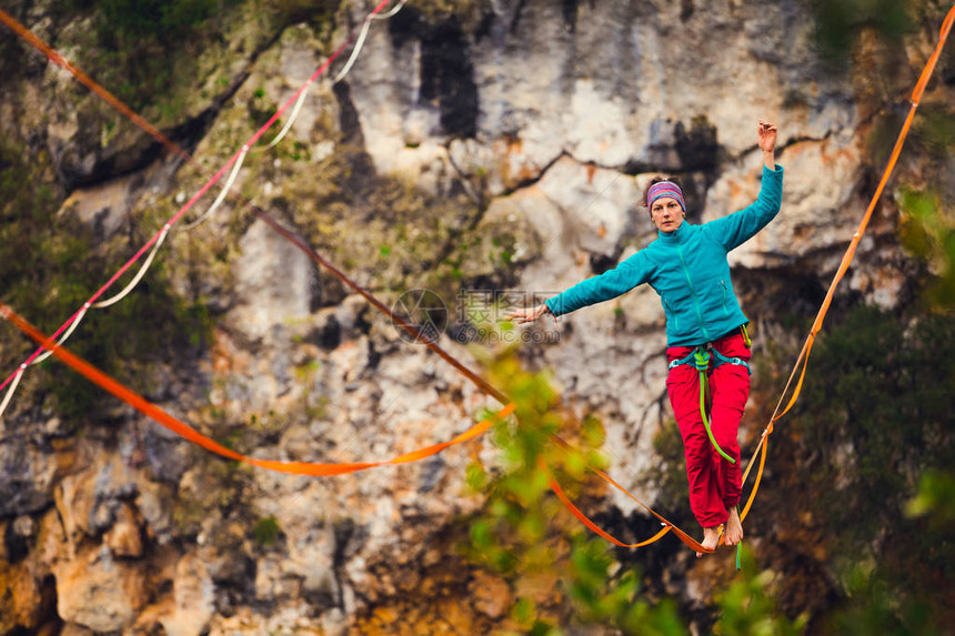 一个女人正沿着一条拉长的吊索行走山中的高线女人抓住了平衡走钢丝者在大自然中的表现雷云背景上的Highliner图片