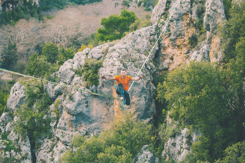 高线山脉的背景一个人坐在拉长的吊索上走钢丝的表演Highliner在深渊上保持平衡运动员摔倒图片