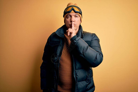 穿着滑雪护目镜在度假的中年帅气的灰发滑雪男子要求用手指对嘴唇保持安静图片