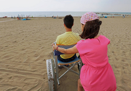 小女孩把特殊的轮椅推到沙滩上夏天和一个图片