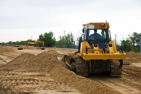 修复旧的和建设新的柏油路在新的道路施工现场工作的挖掘机平图片