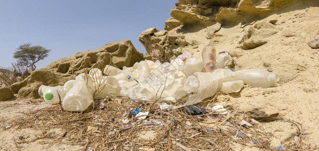 在沙漠中被烧焦的旧塑料垃圾堆在沙漠中的石块和木头背景图片