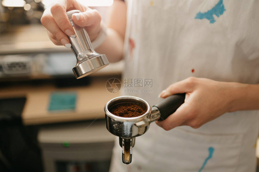 一位女咖啡师在咖啡店里拿着一个金属搅拌器和一个装有咖啡的过滤器咖啡师准备在咖啡馆冲泡浓缩咖图片