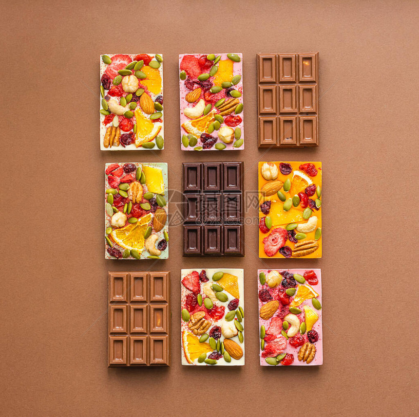各种颜色的巧克力和彩色填料以及棕色背景上的水果坚片顶层视图平面图片