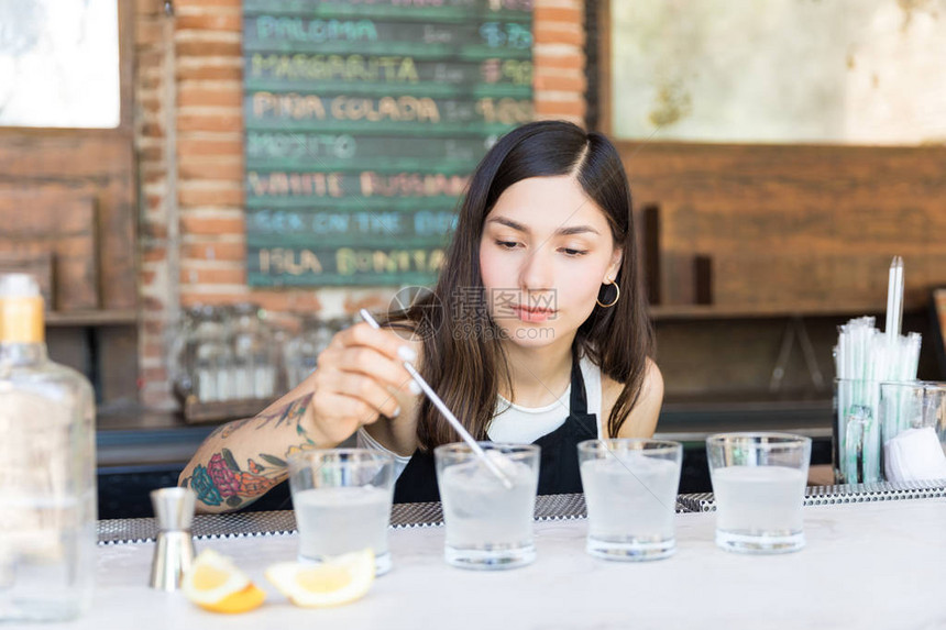 西班牙裔酒吧女招待在酒吧的柜台上用杯图片