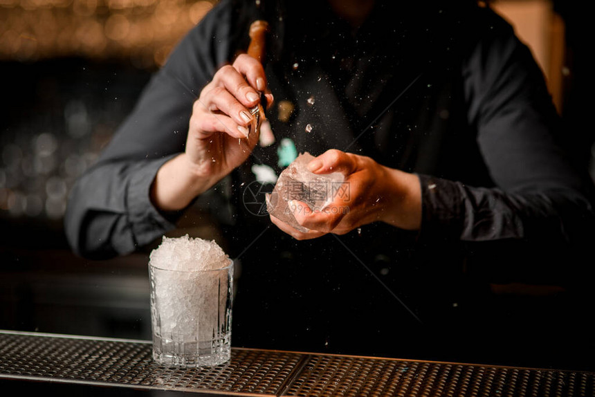 女酒保用特殊的仪器打破大片冰块玻璃和小片的冰架在图片