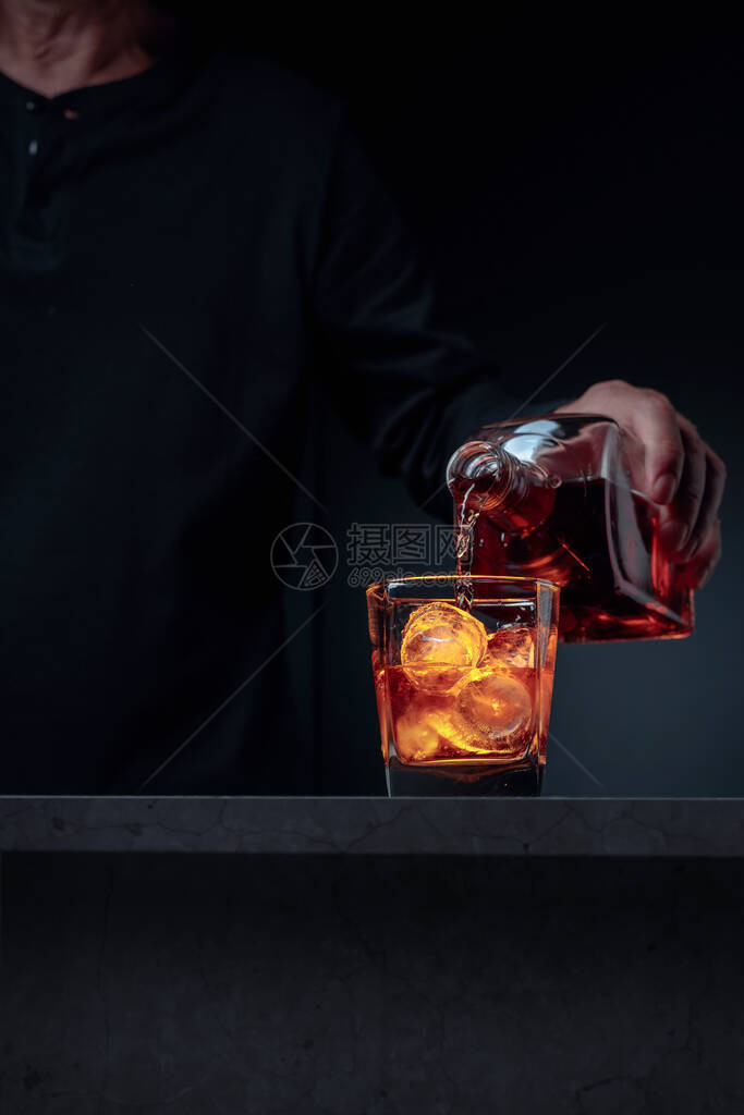酒商把威士忌倒到酒吧柜台的玻璃里酒精饮料从瓶子倒进冰霜杯中有选择的焦图片