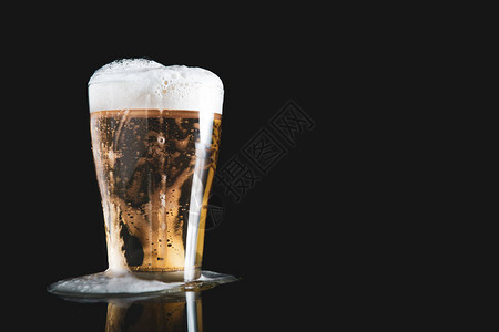 从杯子上倒出的泡沫啤酒黑色背景图片