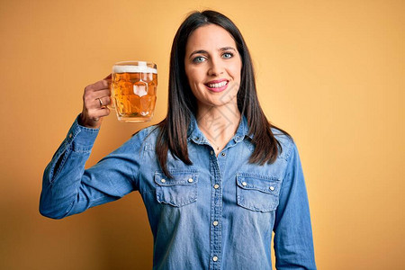 蓝眼睛的年轻女子在孤立的黄色背景上站着喝啤酒罐图片