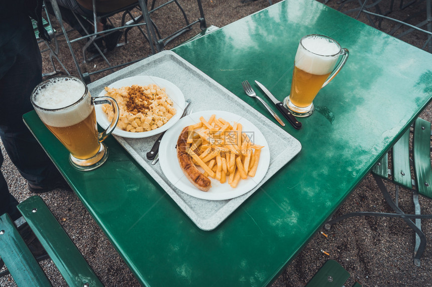 户外用餐区绿色餐桌上的白盘面食炸薯条和香肠快餐的高角度视图图片