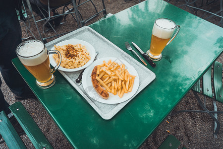 户外用餐区绿色餐桌上的白盘面食炸薯条和香肠快餐的高角度视图图片