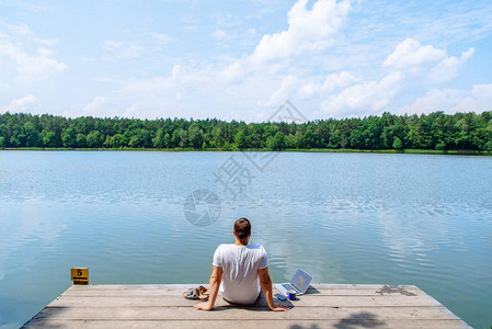 男人坐在笔记本电脑上看湖在度假工背景图片