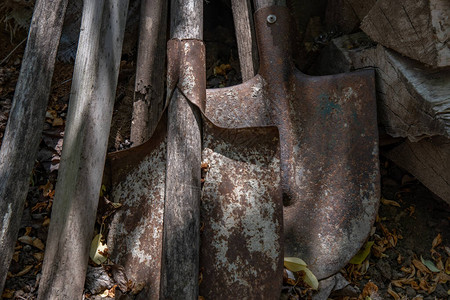 关闭在农场院子里堆积的老旧生锈金属铁铲和肮脏木制板图片