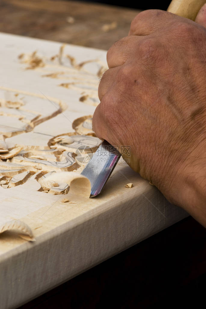 用凿子雕刻木头的工匠的手特写图片