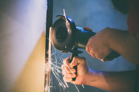 一名男子用人工研磨机修理他家地下室的金属门图片