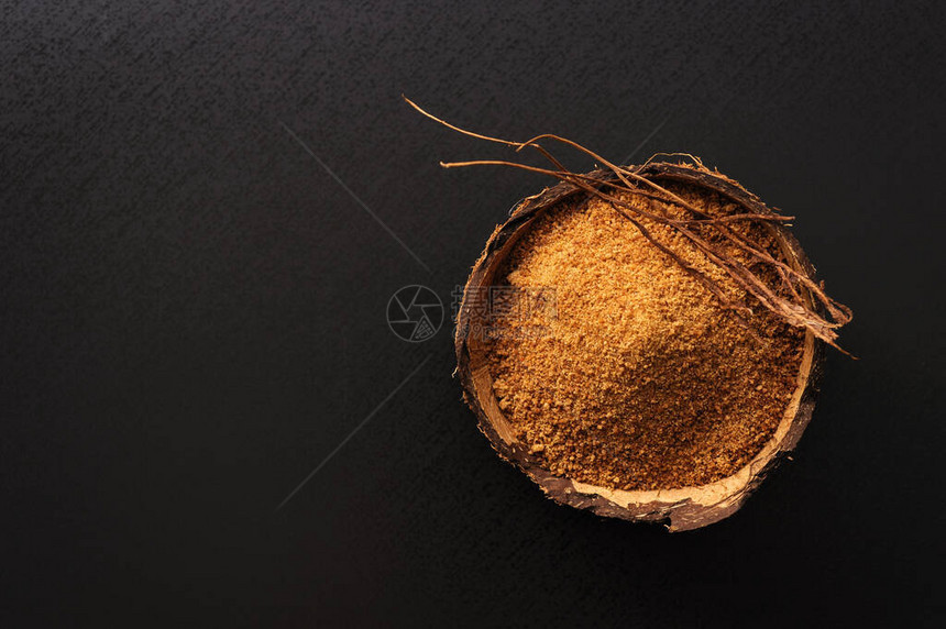 黑色背景的椰子壳中的天然颗粒椰子糖图片