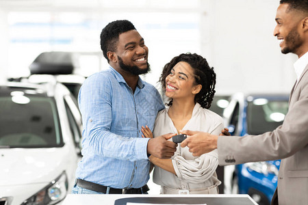 汽车销售经理给站在经销店购买新车的家庭夫妇提供新的汽车钥匙图片