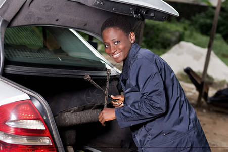 年轻的微笑机修工从车库的汽车后图片