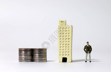 一个迷你男子站在一堆硬币和微型建筑旁边图片