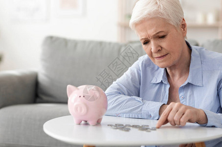 没有退休储蓄心烦的老年妇女从小猪银行中数最后硬币图片