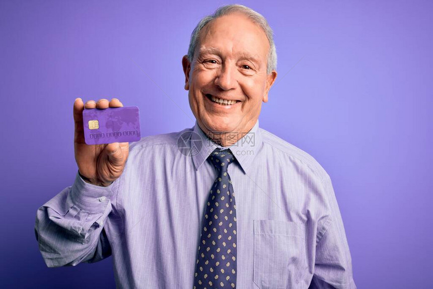 头发灰白的高级商人拿着紫色背景的信用卡图片