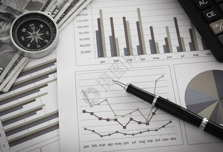 图表上的笔和财务顾问办公桌上带有金钱指南针计算器的图表业务报告会计和背景图片