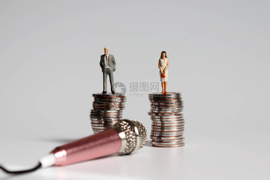 迷你男人和迷你女人站在一块高的硬币上拿着图片