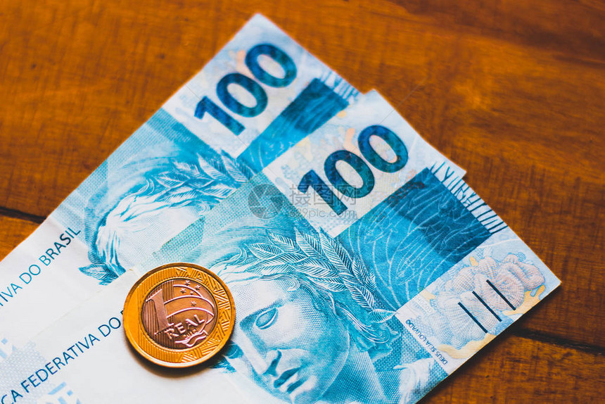 一枚真正的硬币和一百张真正的纸币在木制背景上巴西金钱和薪图片