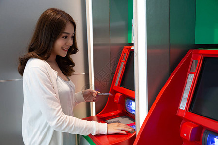 年轻的亚洲女在自动机器上用卡取款图片