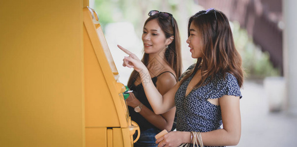 两名美丽的亚洲女在商场用自动取款机从一张图片