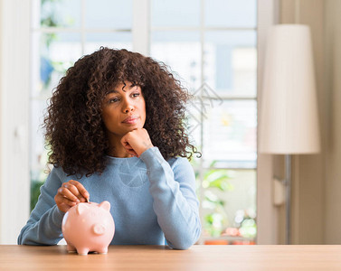 非裔美国女人在小猪银行存钱面对严肃的面孔思考问题图片