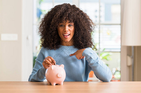 非裔美国女人在小猪银行里存钱却用惊喜的脸面对自己指图片