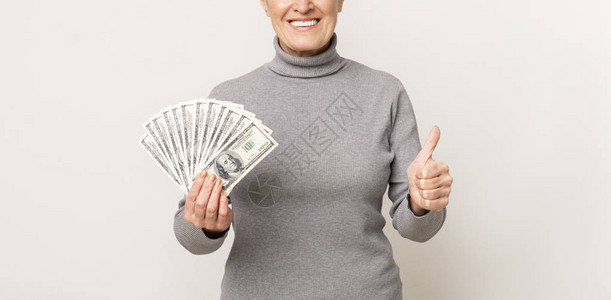 快乐的年长女士拿着一堆钱举起拇指手势图片